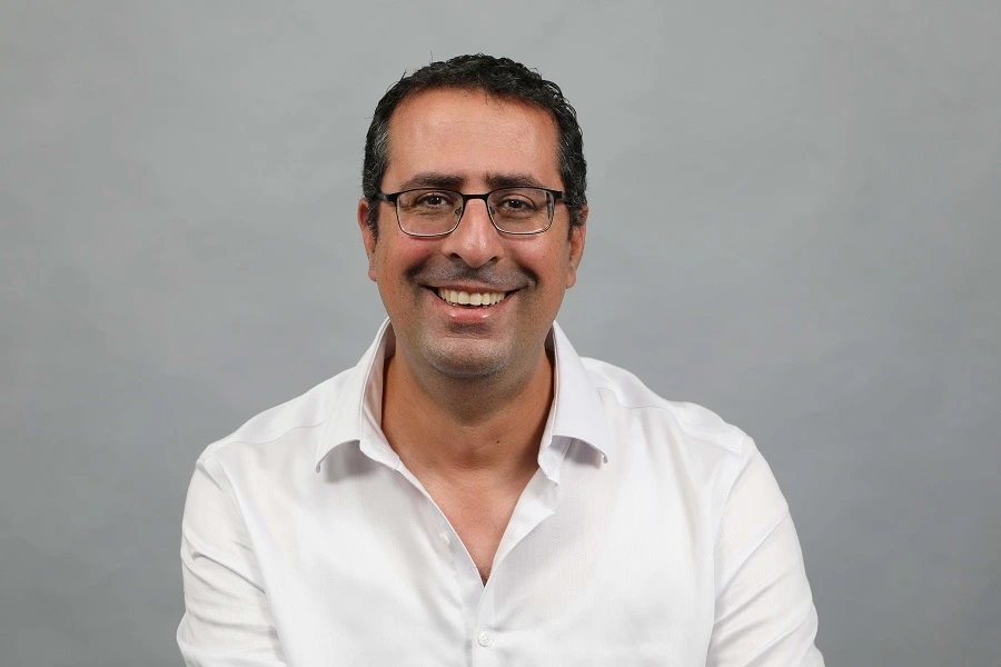 man in a white shirt smiling against a grey wall